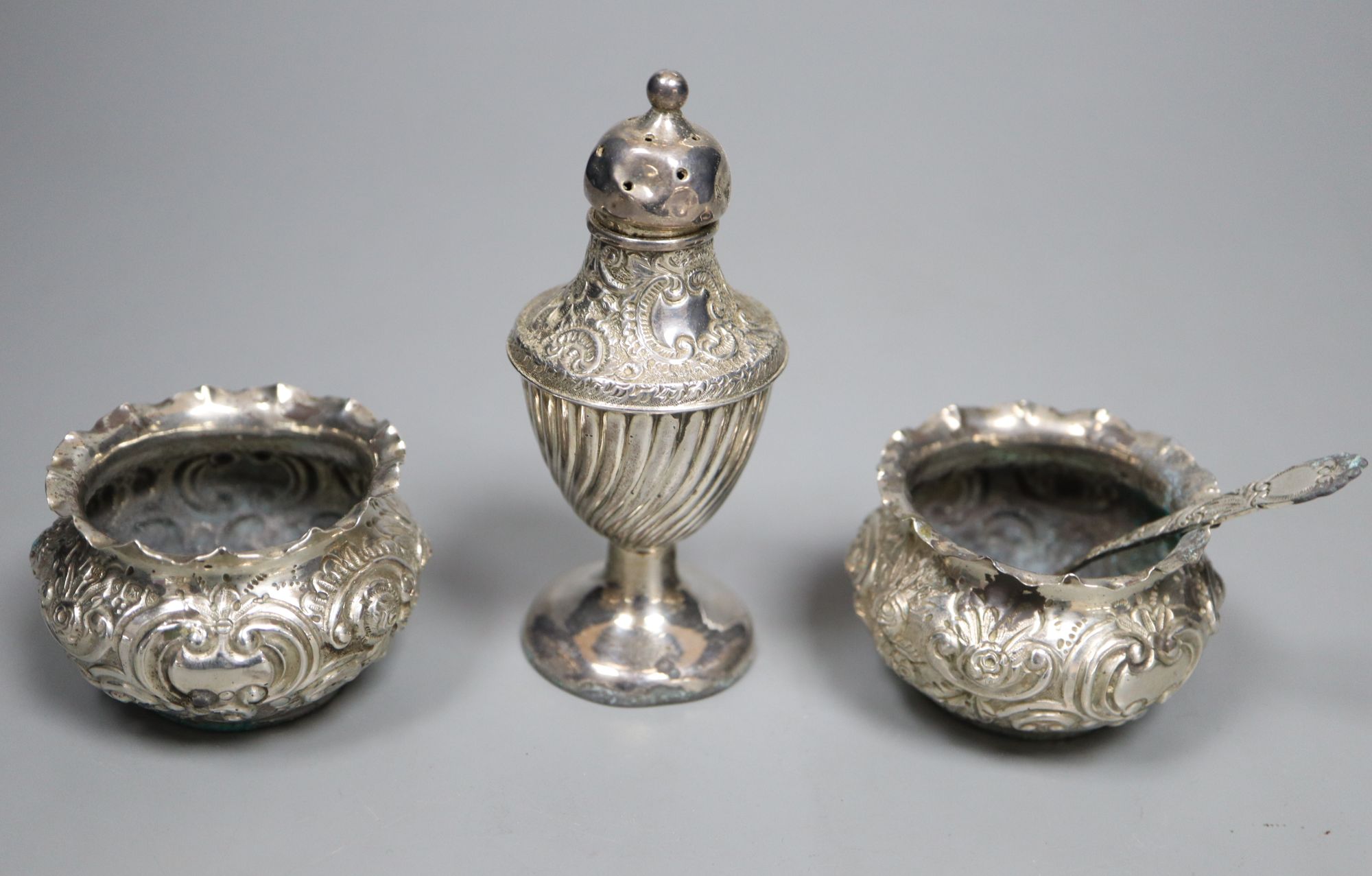 A pair of late Victorian embossed silver salts and one salt spoon, together with a silver mustard pot and a pepper pot (5)